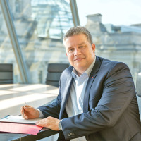 Carsten Träger, MdB, mit Akten in einem Sitzungssaal in Berlin. Im Hintergrund der Reichstag
